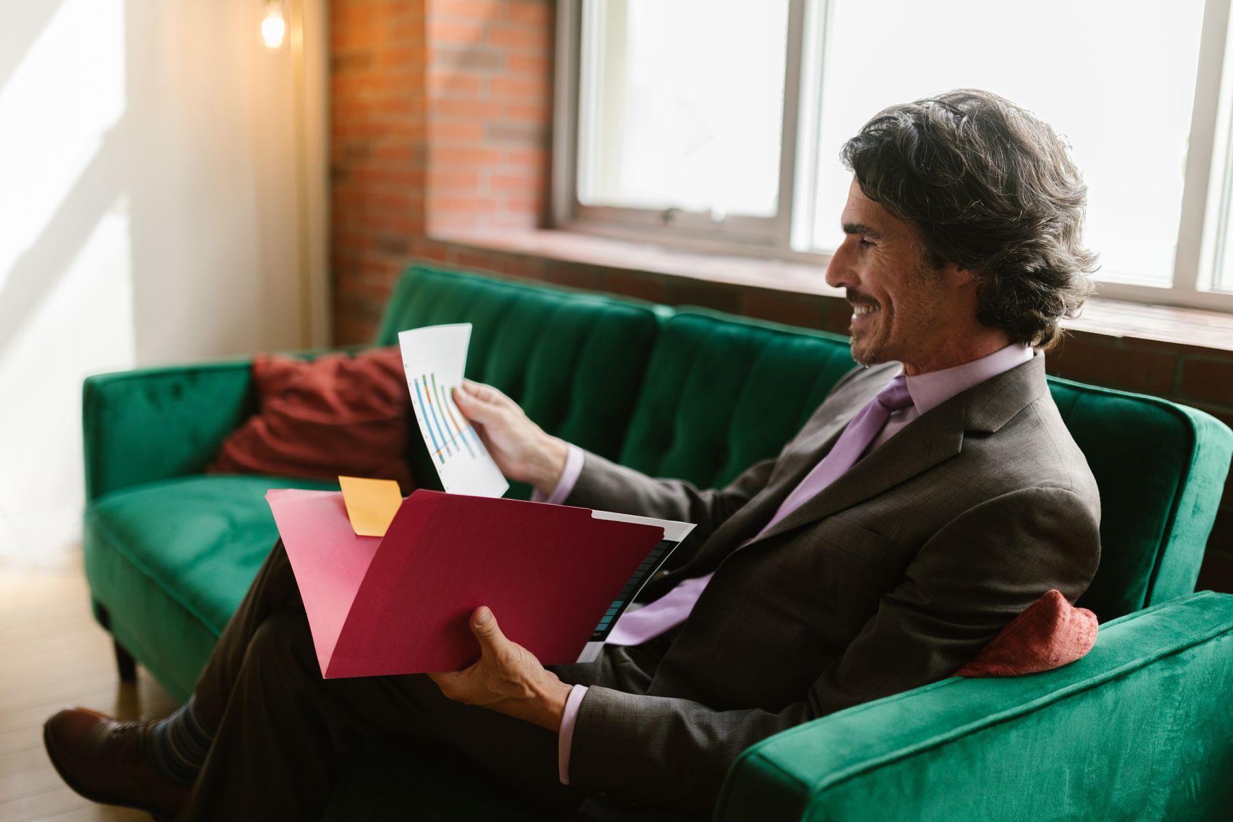 A smiling attorney in a brown suit reviewing documents from a red case folder