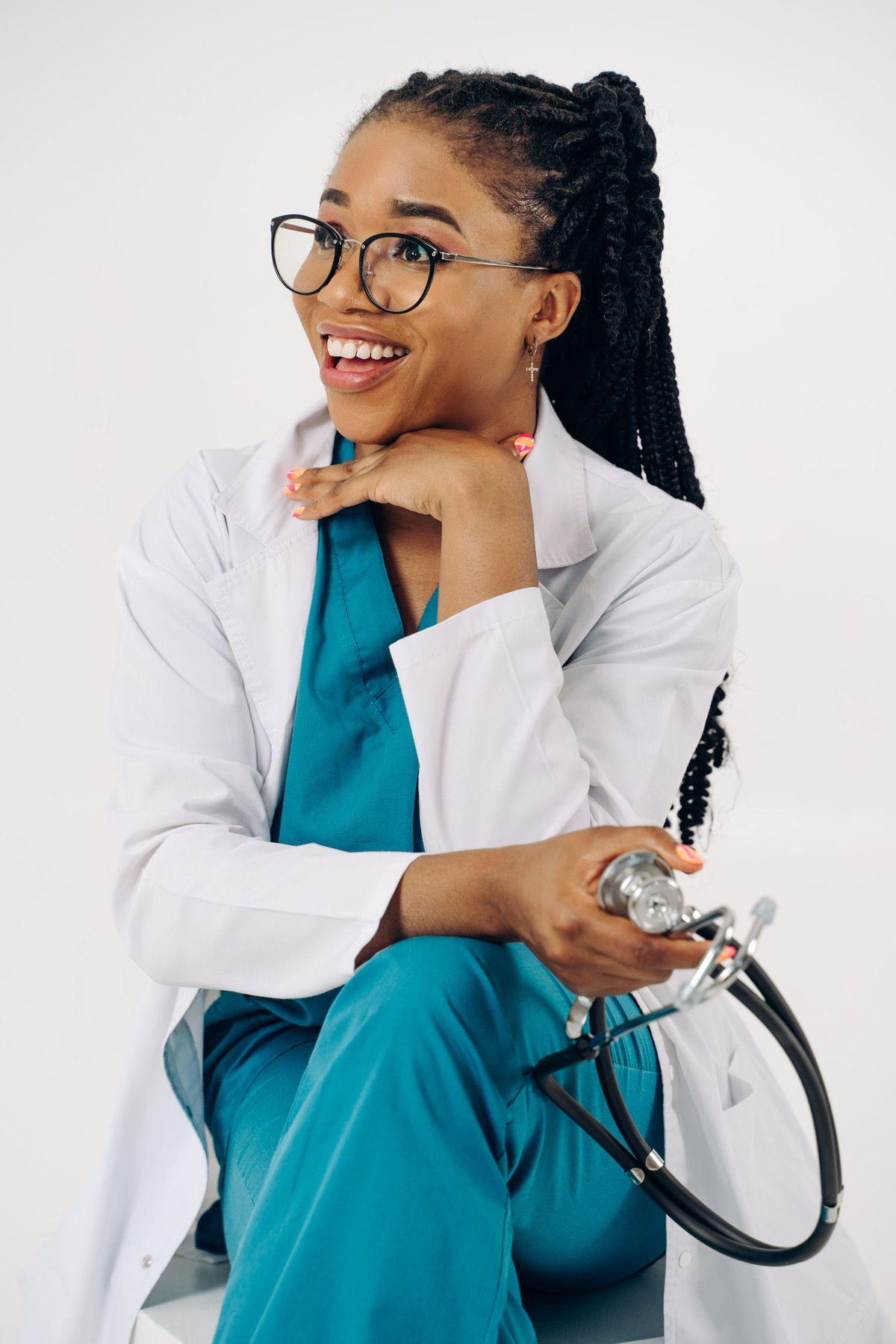 A smiling doctor in teal scrubs and a white coat, holding a stethoscope